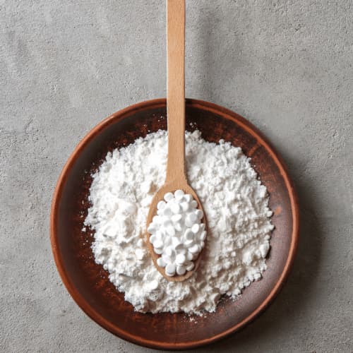 A wooden bowl of granulated white powder, with a spoon on top containing white tablets.