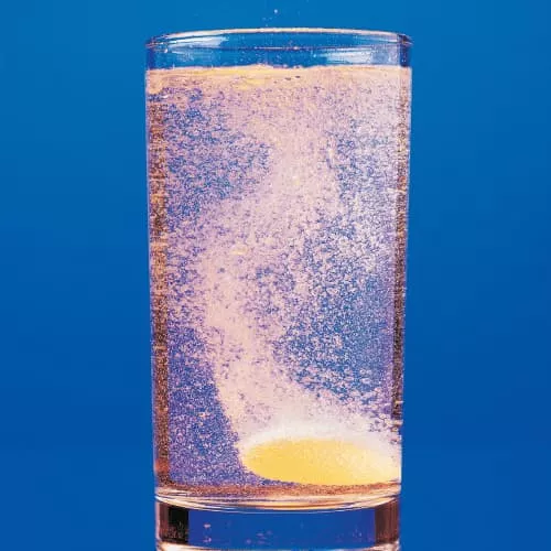 A glass of water with an orange effervescent tablet at the bottom dissolving.
